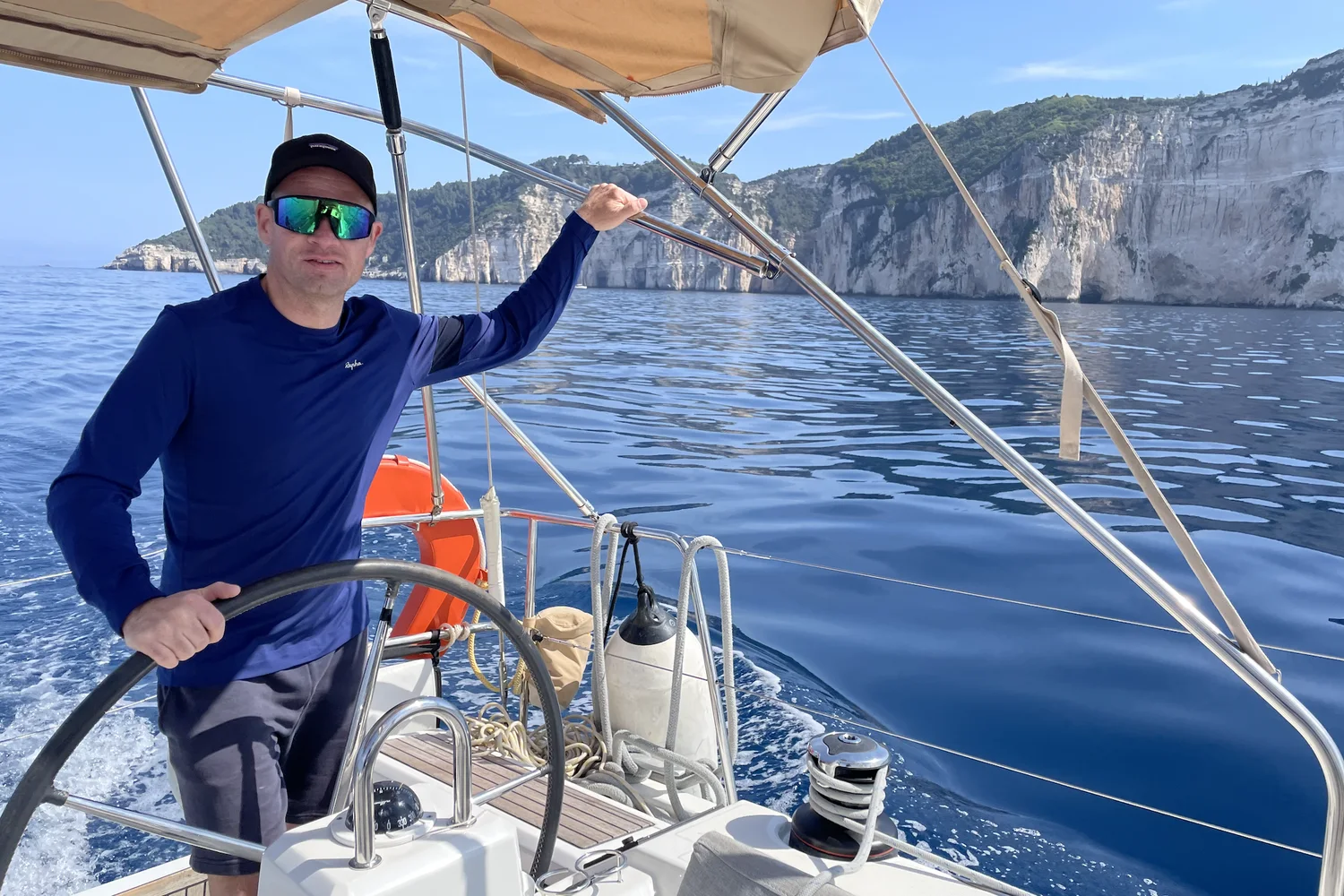 Axel am Steuer einer Segelyacht, im Hintergrund weiße Steilküste und tiefblaues Meer
